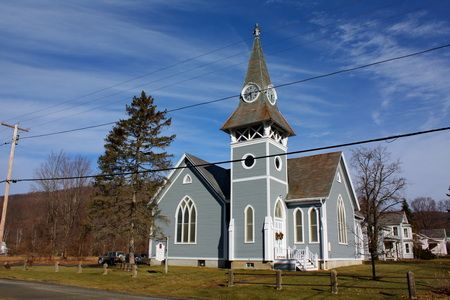 The pale blue clapboard church building with its pointed-arch windows and clock steeple, seen from the road.