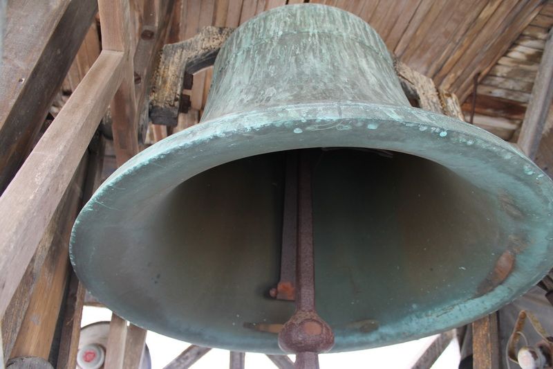 The weathered bronze bell hanging in the church tower, seen from below.