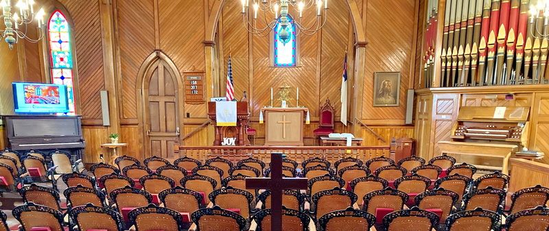 The sanctuary seen from the back: wooden chairs, the chancel and cross, and the painted organ pipes rising on the right-hand wall.