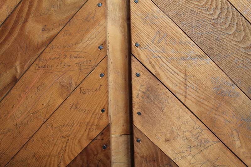The wooden bellows door, its diagonal boards covered in pencilled signatures and dates.